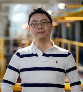 man with dark hair, glasses, and a white shirt with blue stripes