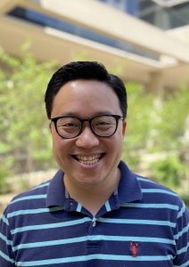Headshot of man with black hair, dark-rimmed glasses, and a blue and teal striped shirt.