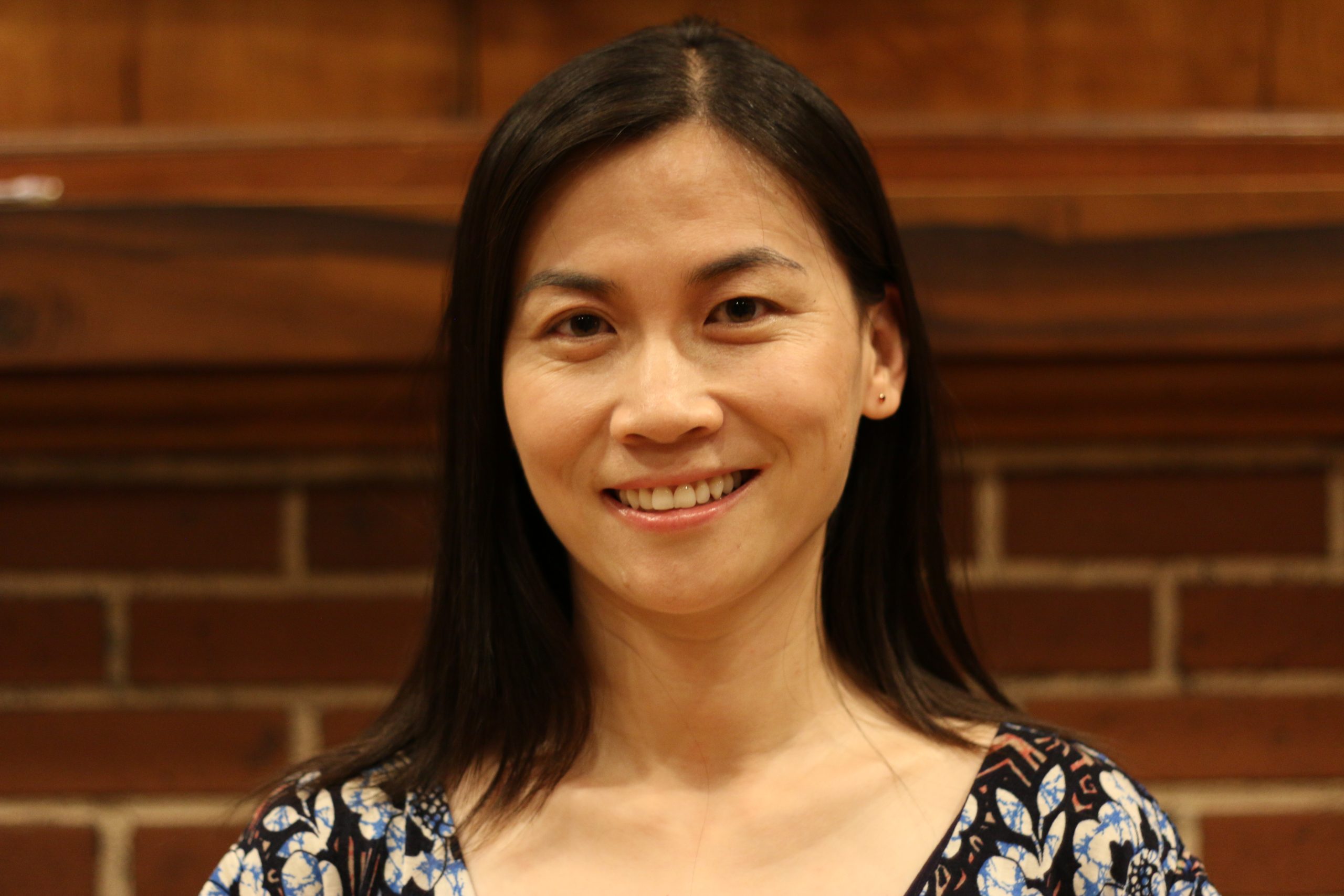 Smiling woman with long dark hair against a brick wall.