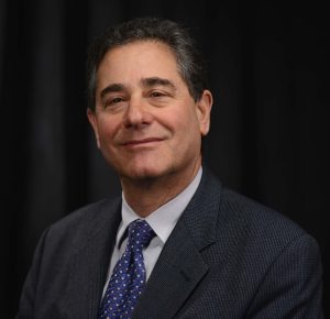 Head shot of a Tom Louis, PhD, a light-skinned man with dark hair wearing a blue suit, dress shirt, and tie
